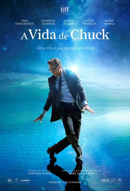 Cartaz de divulgação do filme. Ao centro da imagem, um homem branco, de cabelos curtos e grisalhos, usando óculos de grau, terno azul-marinho, camisa azul-clara, gravata azul-escura e sapatos pretos. Ele está com a perna direita levemente flexionada à frente, a esquerda flexionada para trás, o corpo inclinado para a esquerda, os braços ligeiramente afastados do corpo e as mãos espalmadas para baixo. O fundo é composto por uma paisagem cósmica em tons de azul, com estrelas espalhadas e uma névoa luminosa ao centro. O chão é uma superfície reflexiva que possui pequenas ondulações. Na parte superior do cartaz, em branco, estão listados cinco nomes: “Tom Hiddleston”, “Chiwetel Ejiofor”, “Karen Gillan”, “Com Jacob Tremblay” e “Mark Hamill”. Abaixo, também em branco, o título: “A vida de Chuck”. Logo abaixo do título, em letras menores, está a frase: “Cada vida é um grande universo”. Na base do cartaz, está o logo do Movie Reading. Logo abaixo, estão os símbolos de Audiodescrição, Libras e Closed Caption, além da frase: “Disponível com recursos de acessibilidade”. No canto superior direito, o logo Diamond Films está dentro de um pequeno círculo branco.